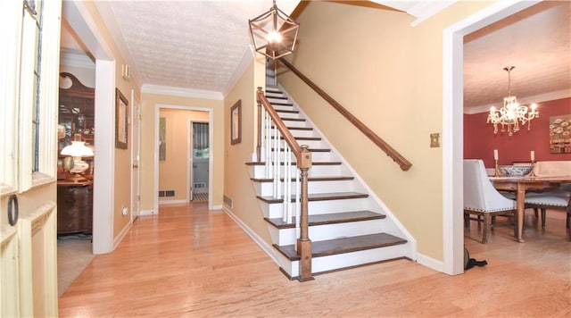 staircase with ornamental molding, hardwood / wood-style floors, and a chandelier