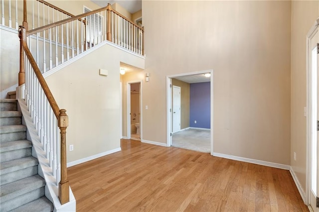 entryway with baseboards, stairs, a towering ceiling, and light wood-style floors