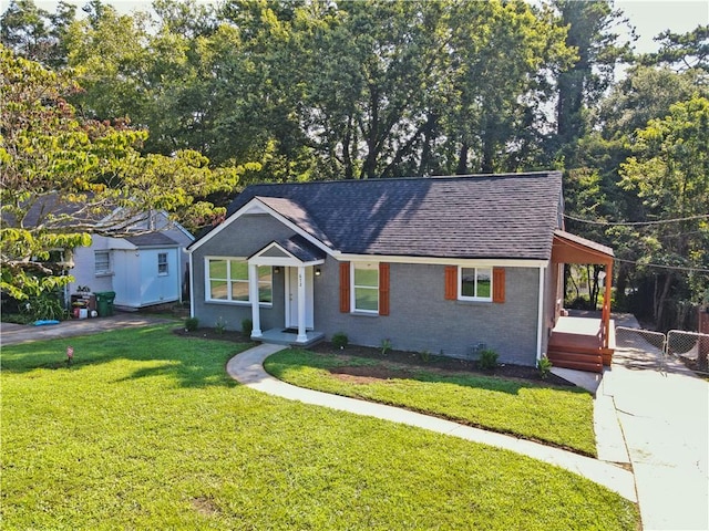 view of front facade featuring a front lawn, a shingled roof, fence, and brick siding