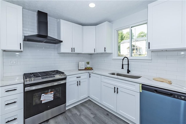 kitchen with gas stove, white cabinetry, a sink, wall chimney range hood, and dishwasher