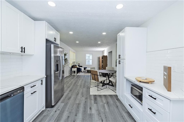 kitchen with light wood finished floors, white cabinets, appliances with stainless steel finishes, light stone countertops, and recessed lighting