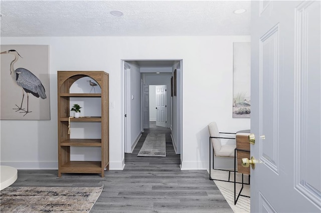 hall with a textured ceiling, wood finished floors, and baseboards