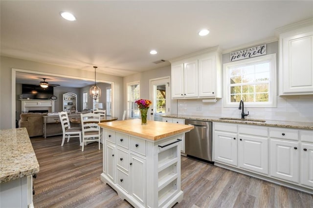 kitchen with dishwasher, butcher block countertops, wood finished floors, a fireplace, and a sink