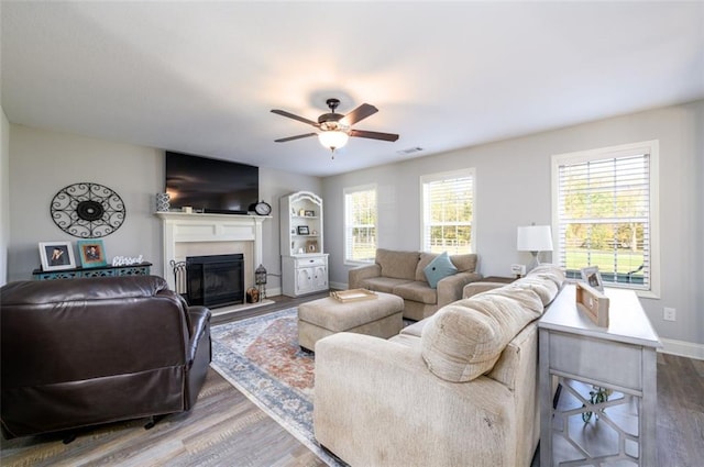 living area featuring baseboards, visible vents, a ceiling fan, a glass covered fireplace, and wood finished floors