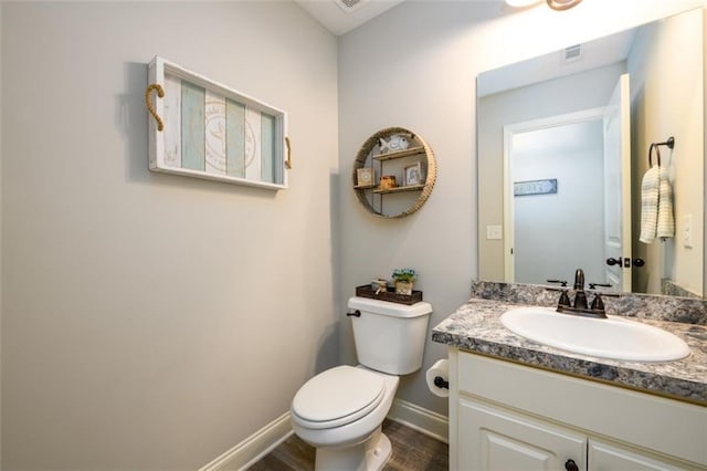 half bath featuring toilet, wood finished floors, vanity, visible vents, and baseboards