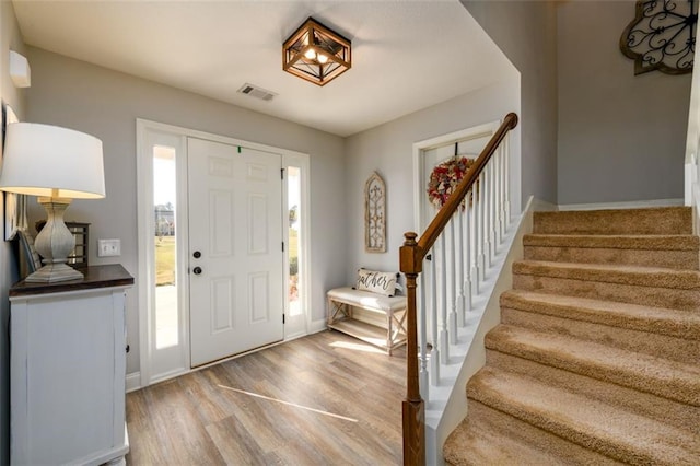 entrance foyer with stairs, wood finished floors, visible vents, and baseboards