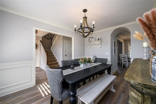 dining area with arched walkways, wainscoting, ornamental molding, dark wood-type flooring, and stairs