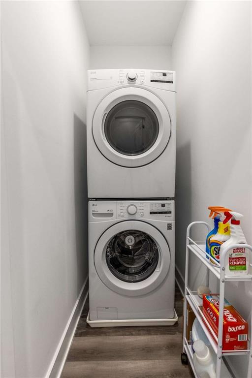 laundry room featuring baseboards, stacked washer / drying machine, wood finished floors, and laundry area