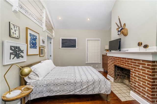 bedroom with lofted ceiling, a brick fireplace, and hardwood / wood-style flooring