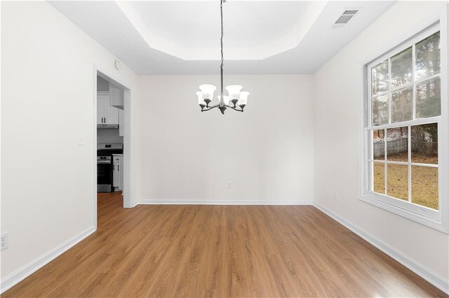 spare room with a raised ceiling, light hardwood / wood-style floors, and an inviting chandelier