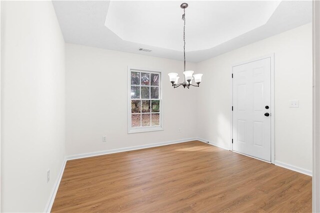 spare room featuring a raised ceiling, wood-type flooring, and a notable chandelier