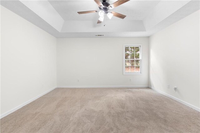 carpeted spare room featuring a raised ceiling and ceiling fan