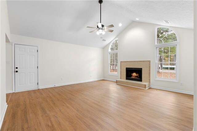 unfurnished living room featuring ceiling fan, light hardwood / wood-style floors, high vaulted ceiling, and a tiled fireplace