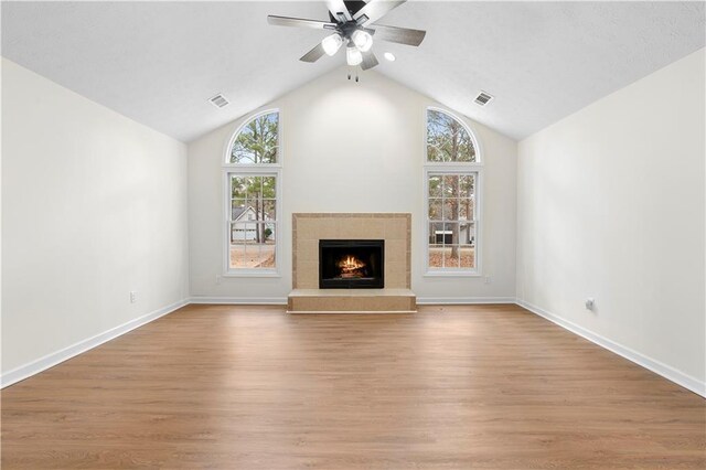 unfurnished living room with light hardwood / wood-style floors, vaulted ceiling, ceiling fan, and a tiled fireplace