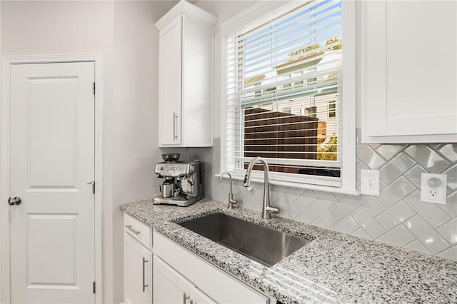 kitchen with backsplash, light stone countertops, sink, and white cabinets