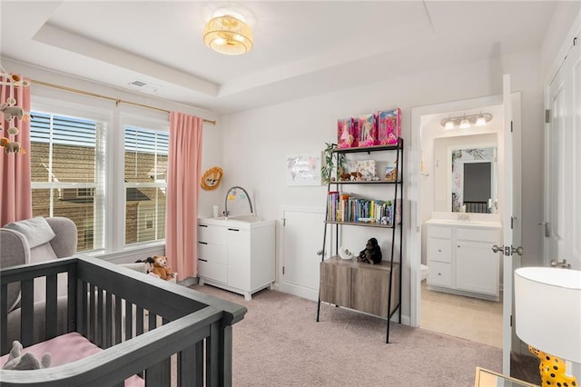 bedroom featuring a raised ceiling, connected bathroom, a crib, sink, and light colored carpet