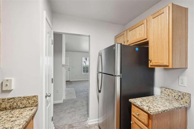 kitchen featuring stainless steel refrigerator, light stone counters, light brown cabinetry, and light carpet