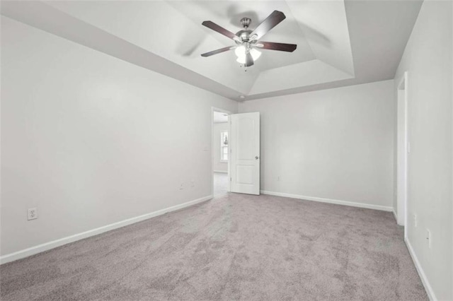 carpeted spare room with a tray ceiling and ceiling fan