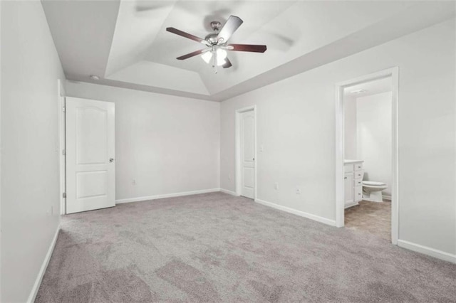 unfurnished bedroom with ceiling fan, a raised ceiling, light carpet, and ensuite bath