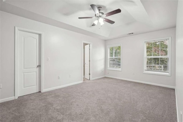 empty room featuring light carpet, a tray ceiling, and ceiling fan