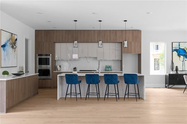 1610 Niskey Lake Rd, Atlanta, GA 30331 - kitchen featuring modern cabinets, stainless steel double oven, light wood-style flooring, light countertops, and a large island