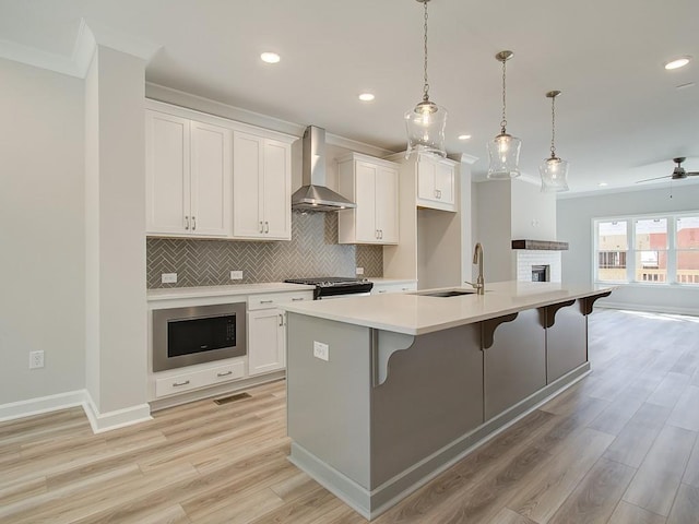 kitchen with white cabinets, wall chimney exhaust hood, sink, a kitchen island with sink, and built in microwave