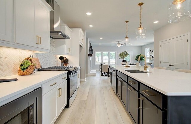 kitchen with ceiling fan, white cabinets, decorative light fixtures, an island with sink, and stainless steel appliances