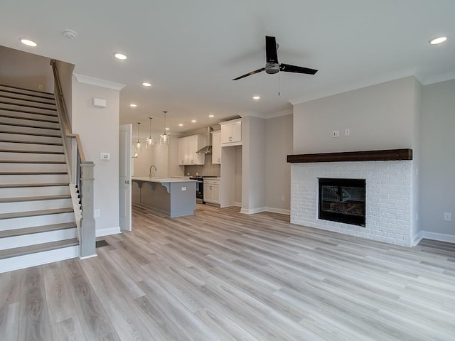 unfurnished living room with a brick fireplace, light hardwood / wood-style floors, sink, ceiling fan, and crown molding