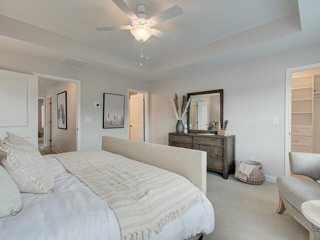 carpeted bedroom featuring ceiling fan, multiple windows, and a tray ceiling