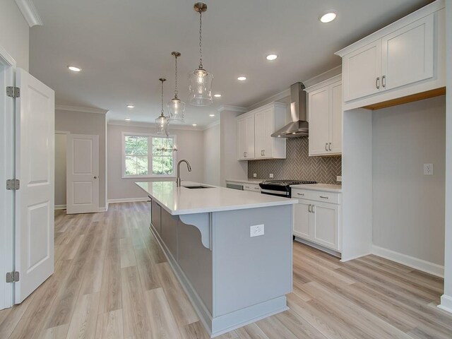 kitchen with sink, gas stove, pendant lighting, a center island with sink, and wall chimney exhaust hood