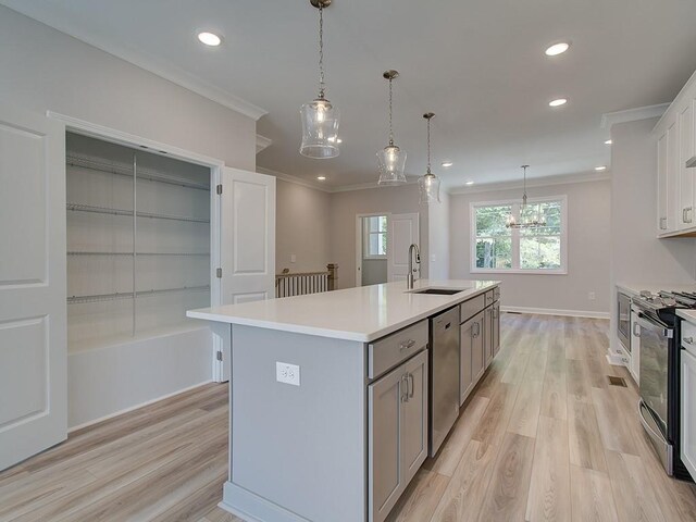 kitchen with pendant lighting, sink, wall chimney exhaust hood, an island with sink, and gas stove