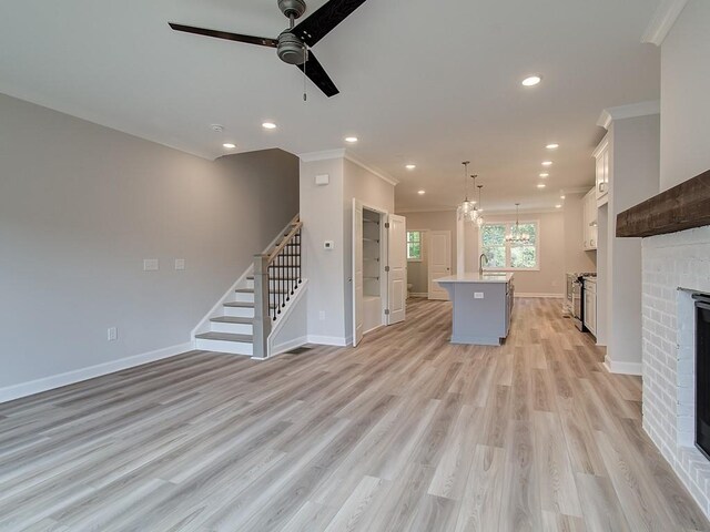 unfurnished living room with ceiling fan, light wood-type flooring, crown molding, and a fireplace