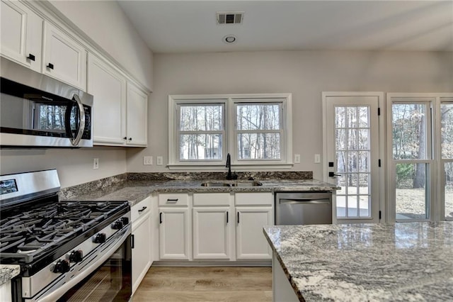 kitchen with white cabinetry, appliances with stainless steel finishes, light stone countertops, and sink