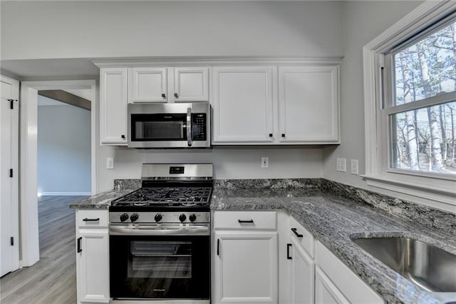 kitchen with white cabinetry, appliances with stainless steel finishes, light wood-type flooring, and dark stone counters