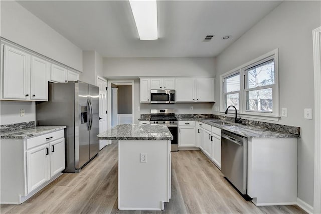 kitchen featuring a kitchen island, appliances with stainless steel finishes, sink, white cabinets, and light stone counters