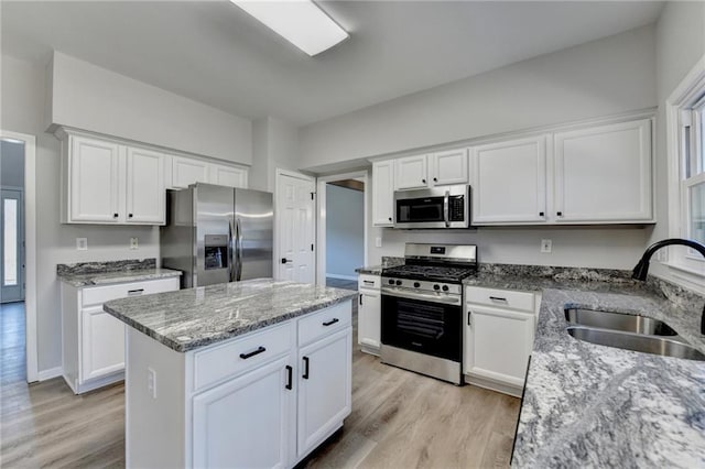 kitchen with a kitchen island, appliances with stainless steel finishes, sink, white cabinets, and light stone counters