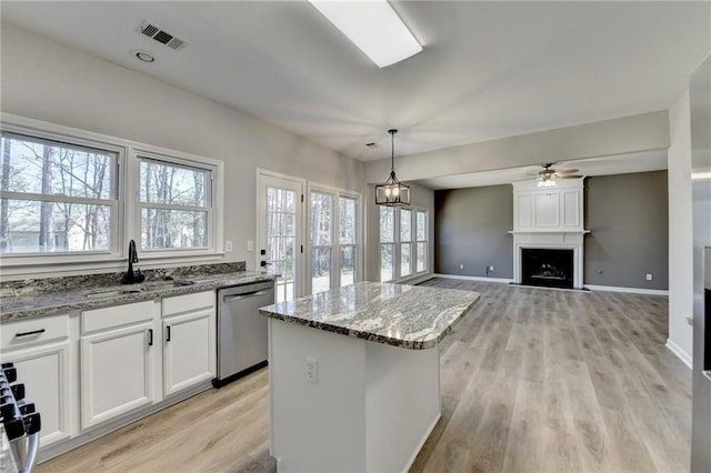 kitchen featuring stone counters, a kitchen island, sink, white cabinets, and stainless steel dishwasher