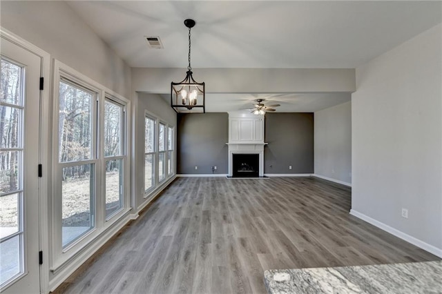 unfurnished living room featuring wood-type flooring, ceiling fan with notable chandelier, and a fireplace