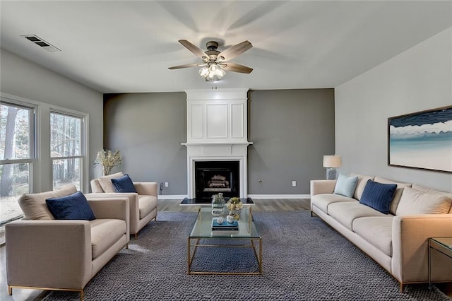 living room with ceiling fan, a large fireplace, and dark hardwood / wood-style floors