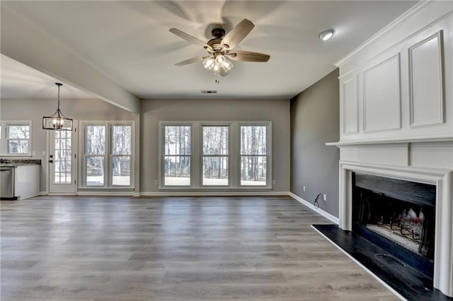 unfurnished living room with ceiling fan with notable chandelier, a fireplace, and light hardwood / wood-style floors