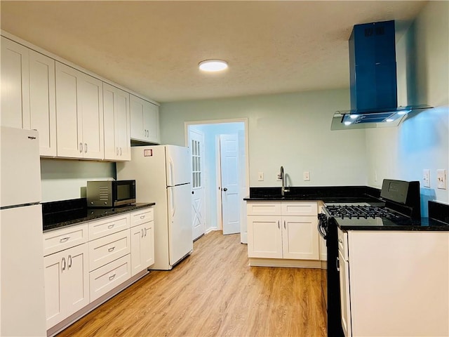 kitchen featuring white fridge, gas range oven, white cabinetry, and extractor fan