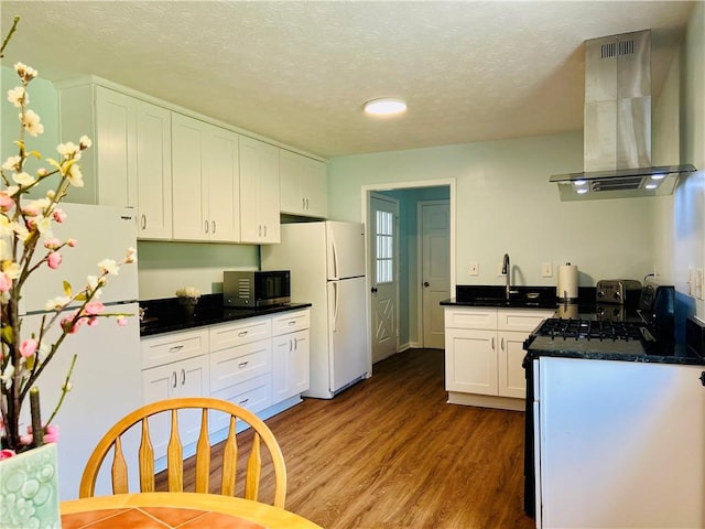 kitchen featuring a textured ceiling, wall chimney range hood, white refrigerator, white cabinets, and hardwood / wood-style floors