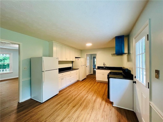 kitchen with white cabinetry, light hardwood / wood-style flooring, white fridge, and wall chimney range hood