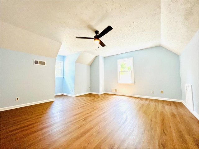 additional living space featuring a textured ceiling, light hardwood / wood-style flooring, ceiling fan, and vaulted ceiling