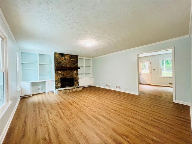 unfurnished living room with built in features, crown molding, wood-type flooring, a textured ceiling, and a fireplace