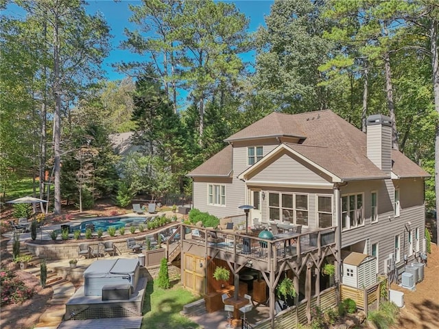 rear view of house with roof with shingles, a chimney, an outdoor pool, and a wooden deck