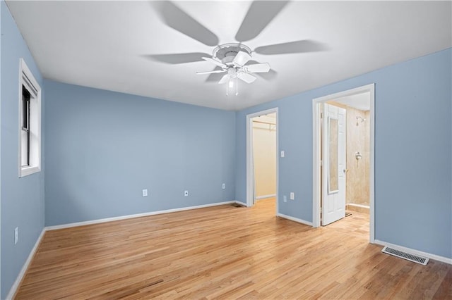 unfurnished bedroom featuring ensuite bath, ceiling fan, a walk in closet, a closet, and light wood-type flooring