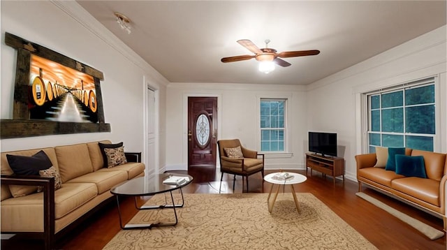 living area featuring dark wood-type flooring, ceiling fan, crown molding, and baseboards