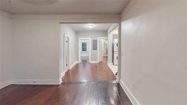 hallway featuring stacked washer and clothes dryer, hardwood / wood-style floors, baseboards, and electric panel