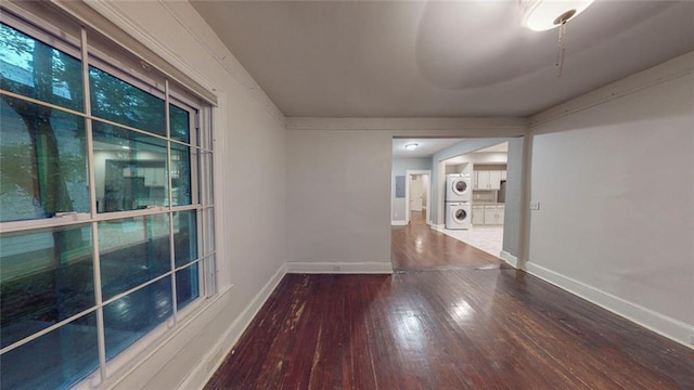 spare room with stacked washer / drying machine, hardwood / wood-style floors, and baseboards